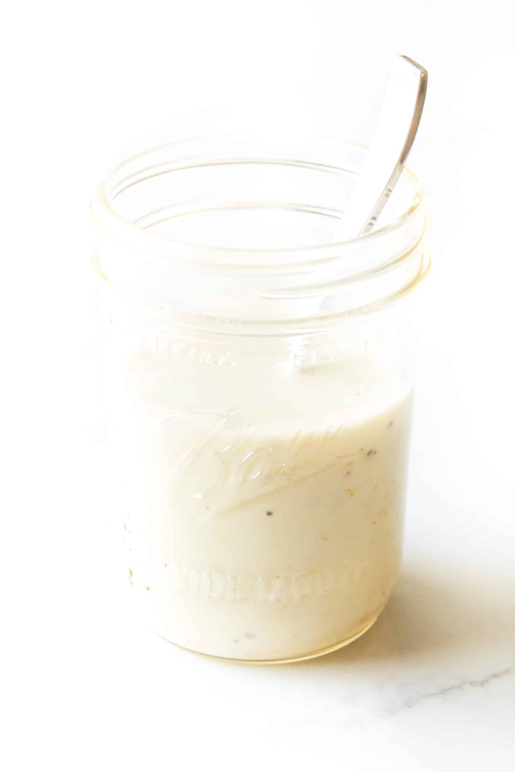 white lemon garlic aioli sauce in a mason jar with a spoon inside on a white background