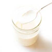 spoon pouring a white sauce into a mason jar on a white background