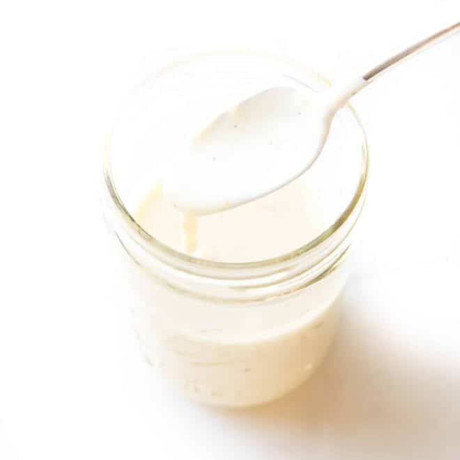 spoon pouring a white sauce into a mason jar on a white background
