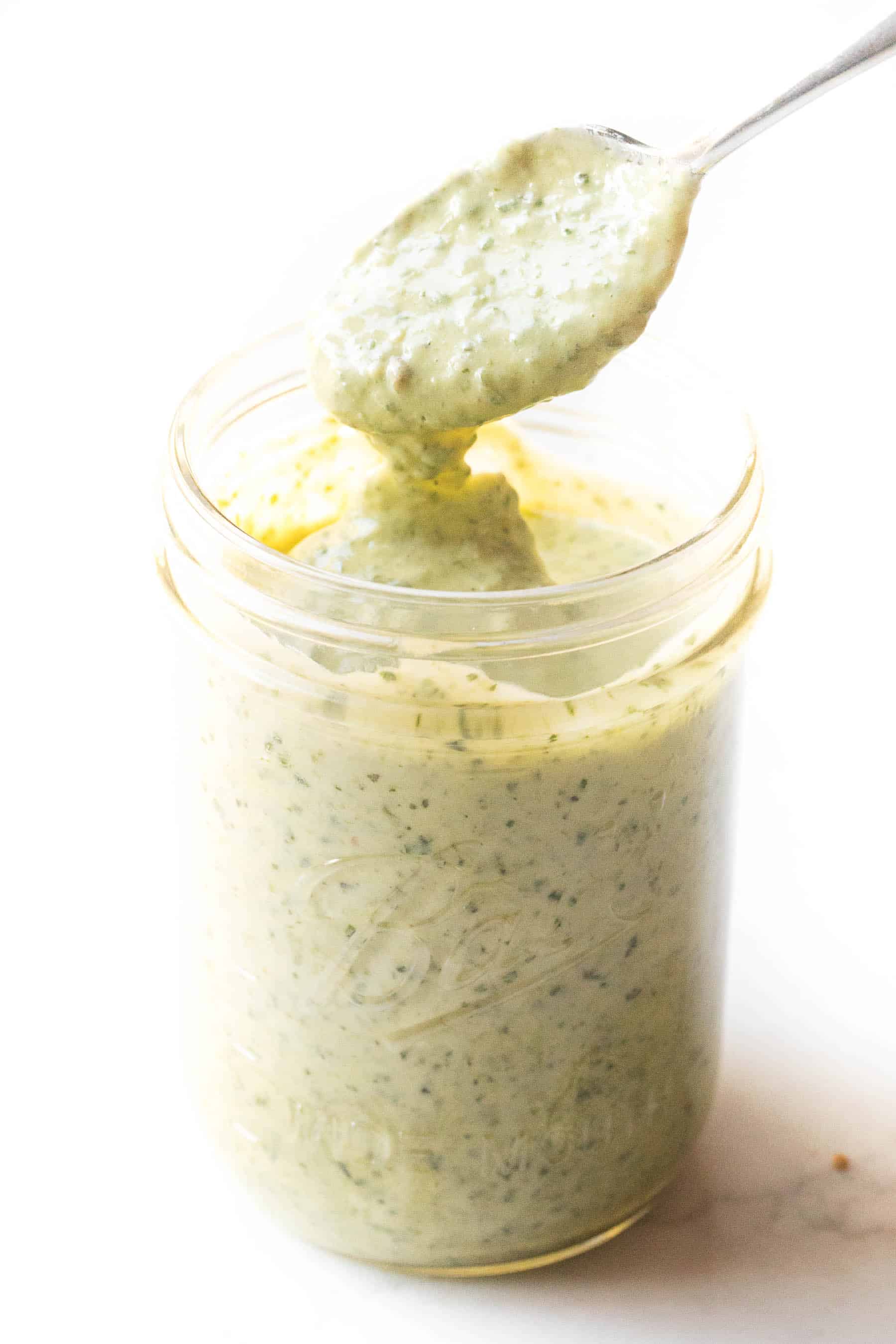 Spoon dripping pesto aioli into a mason jar on a white background