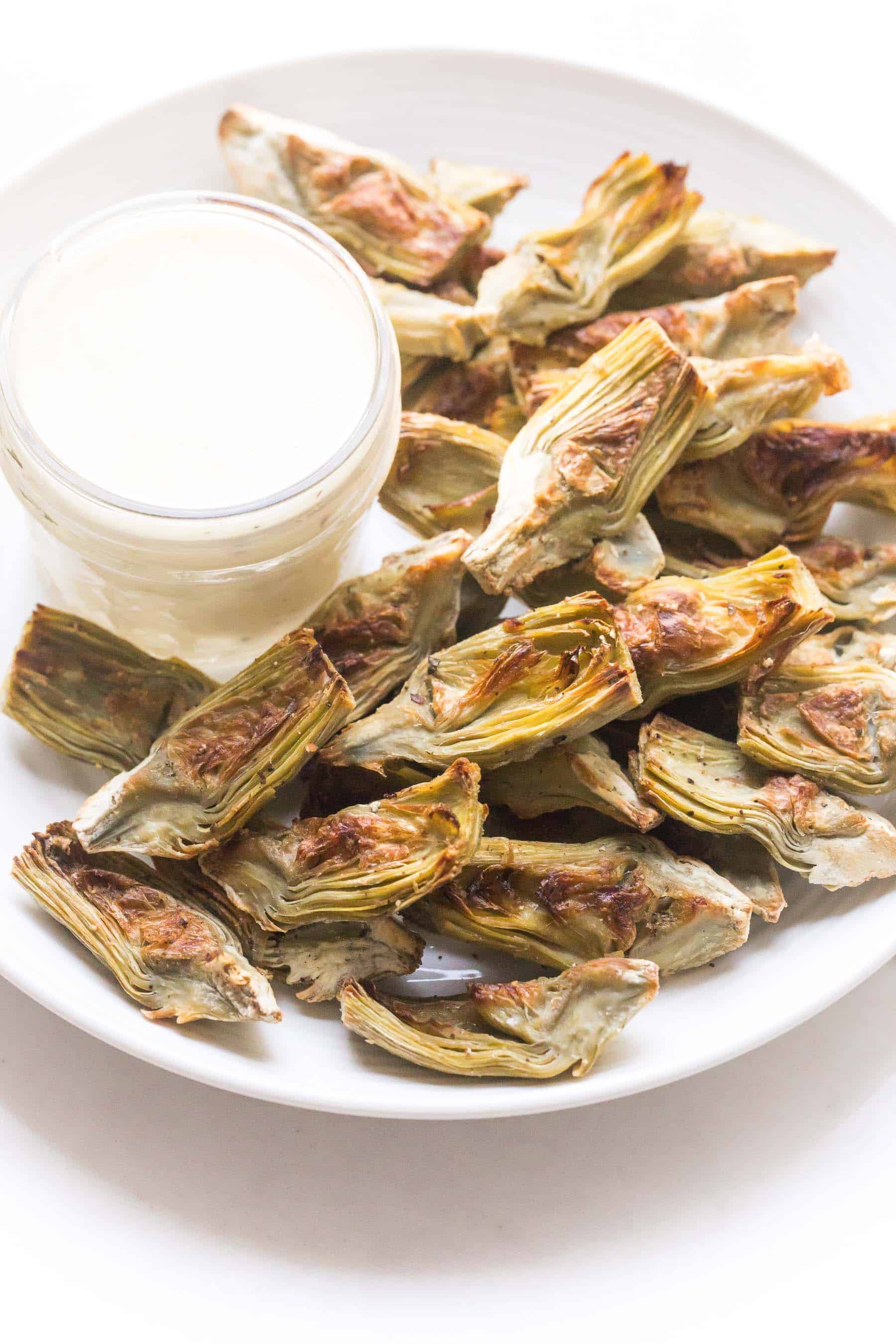 roasted artichoke hearts on a white plate with lemon garlic aioli dipping sauce on a white background