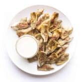 roasted artichokes on a white plate with a white dip on a white background