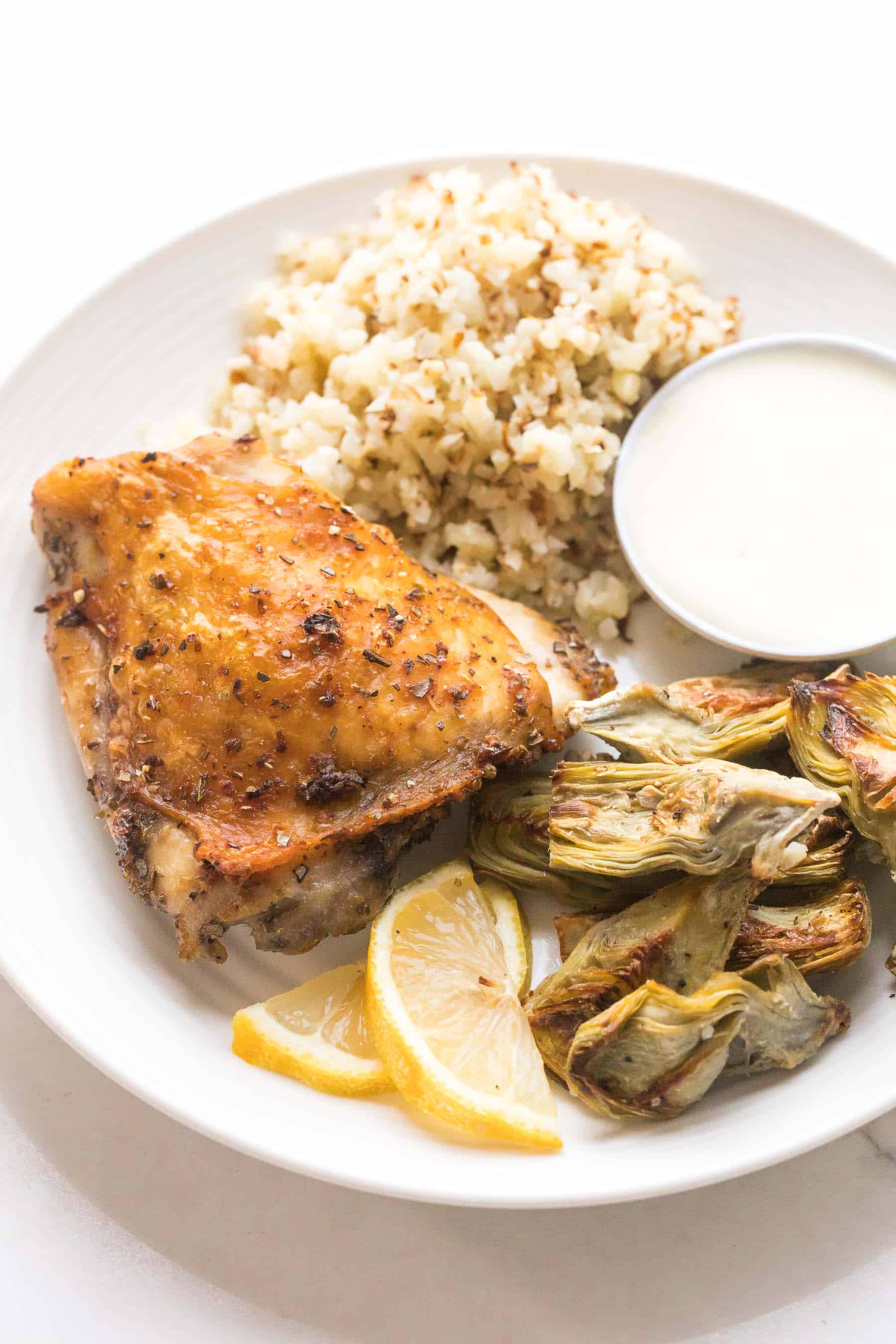 roasted chicken thigh, artichokes and cauliflower rice on a white plate