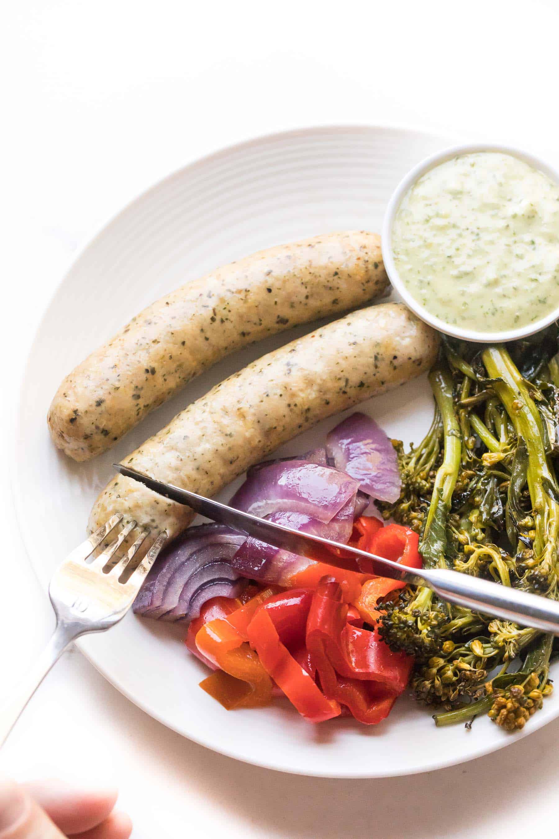 knife cutting sausages and vegetables on a white plate on a white background