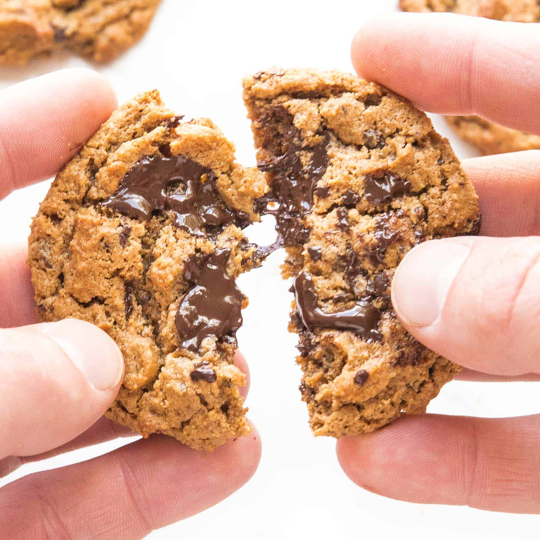 a hand breaking apart a chocolate chip cookie 