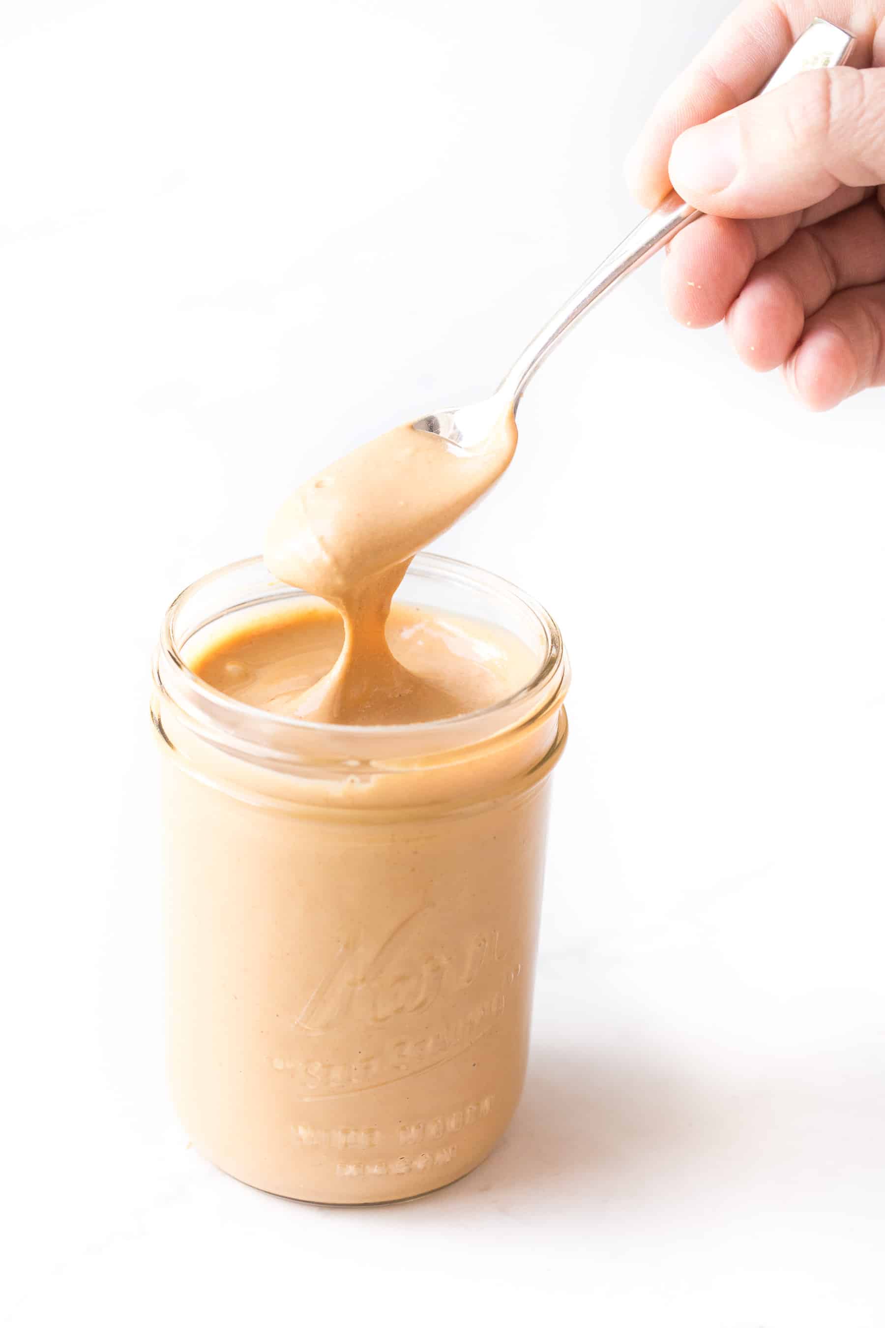 spoon pouring cashew butter into a mason jar