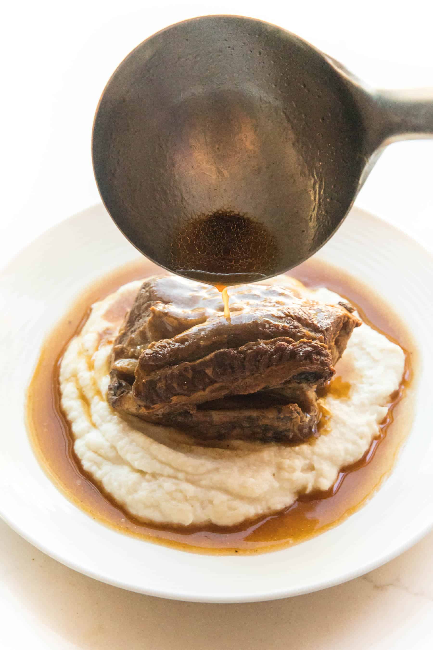 pouring sauce over short ribs and mashed cauliflower
