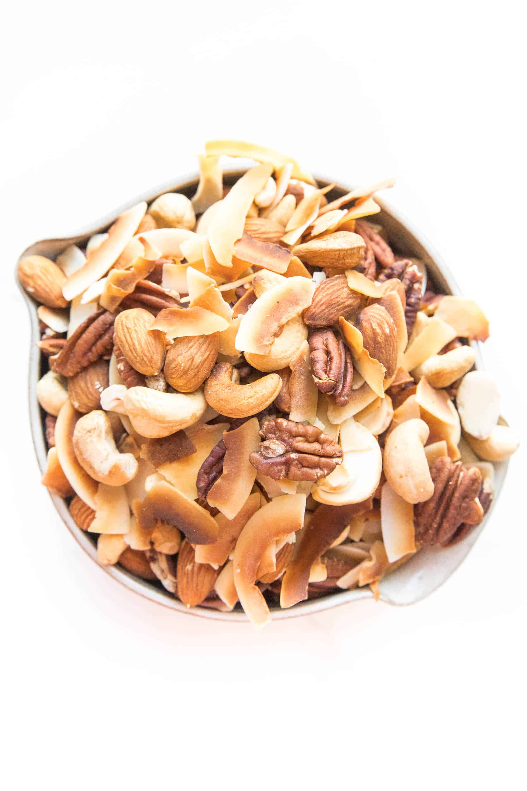 nuts and coconut chips trail mix in a bowl on white background