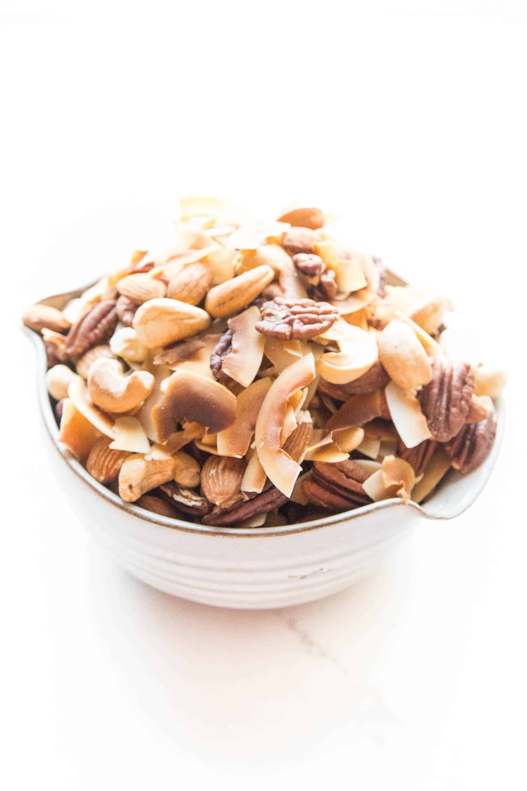 nuts and coconut chips trail mix in a bowl on white background