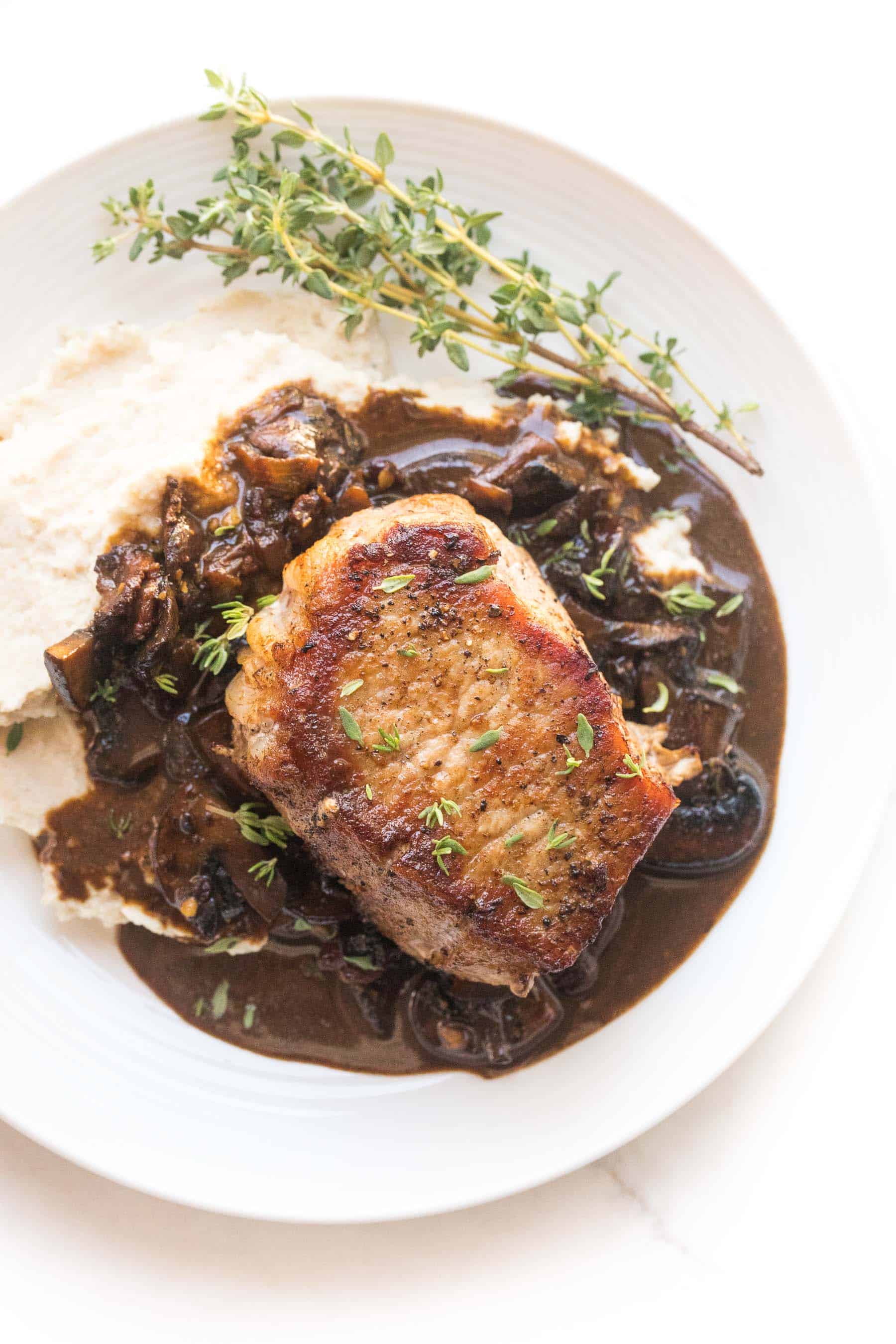 pork chops with bacon mushroom sauce and mashed cauliflower with fresh thyme on a white plate and white background