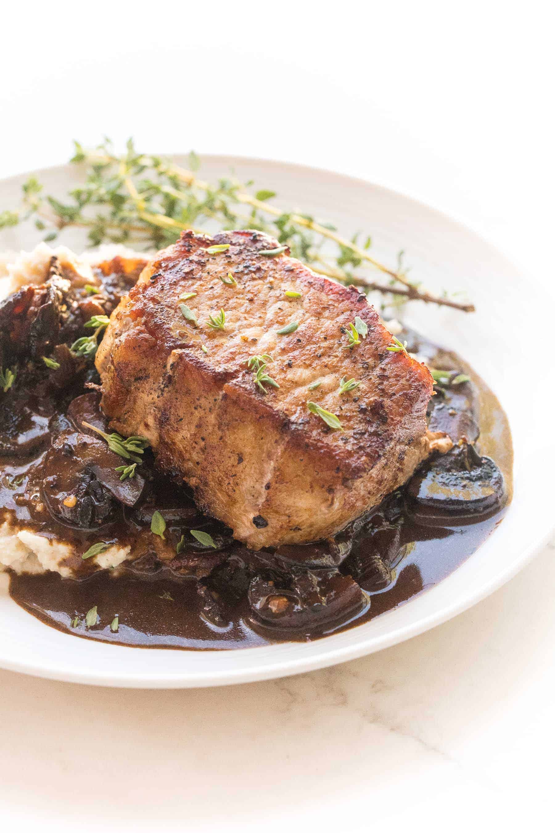 pork chops with bacon mushroom sauce and mashed cauliflower with fresh thyme on a white plate and white background