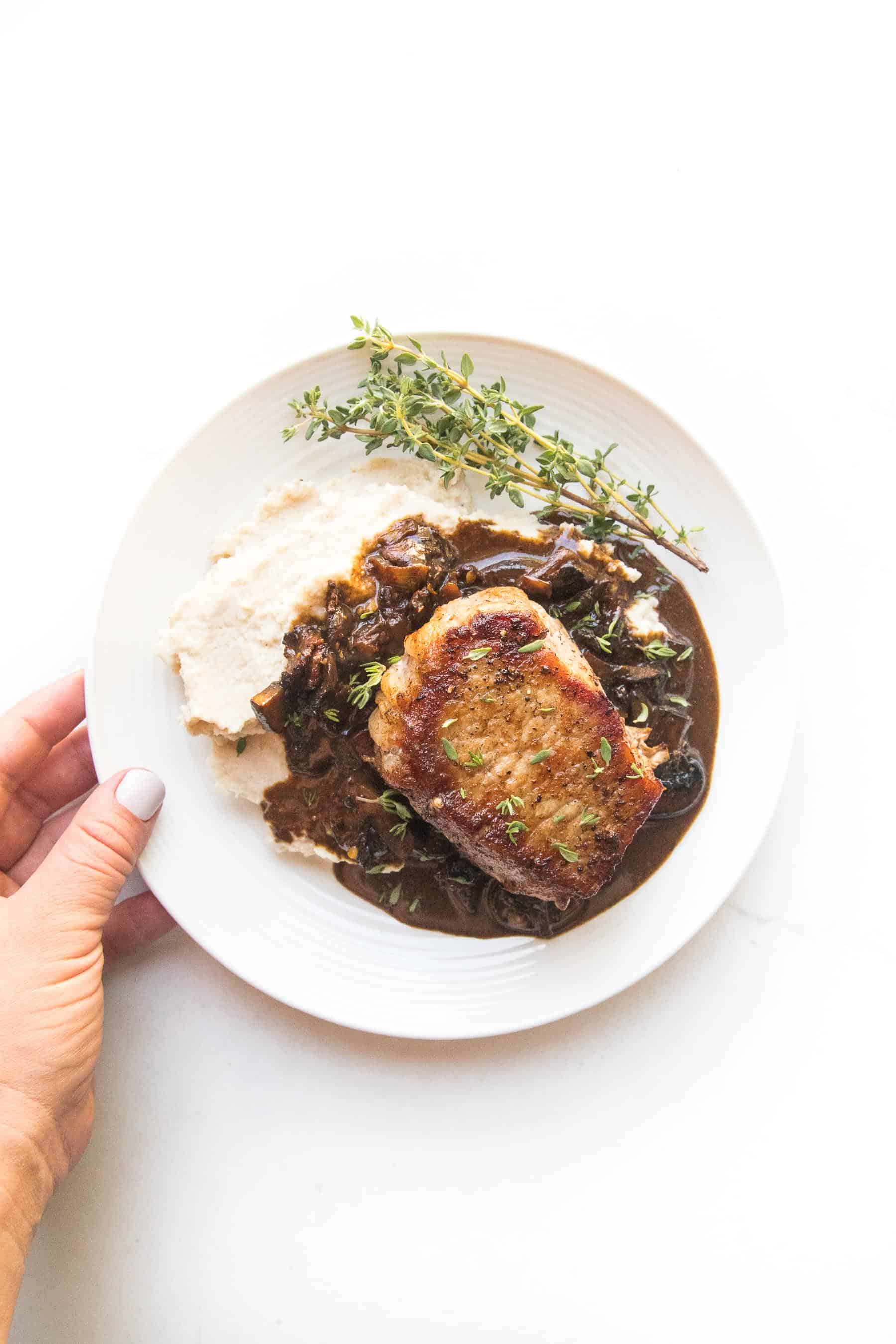 pork chops with bacon mushroom sauce and mashed cauliflower with fresh thyme on a white plate and white background