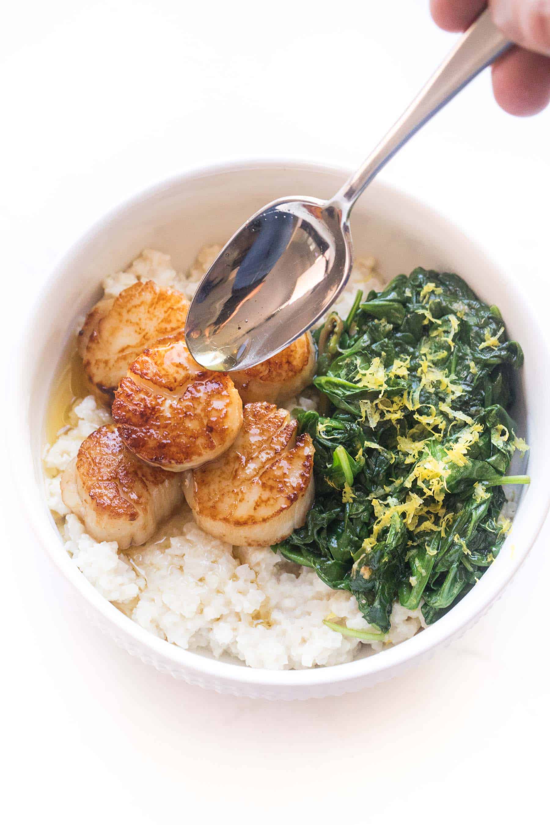 Seared scallops in a white bowl with cauliflower rice risotto + sauteed spinach