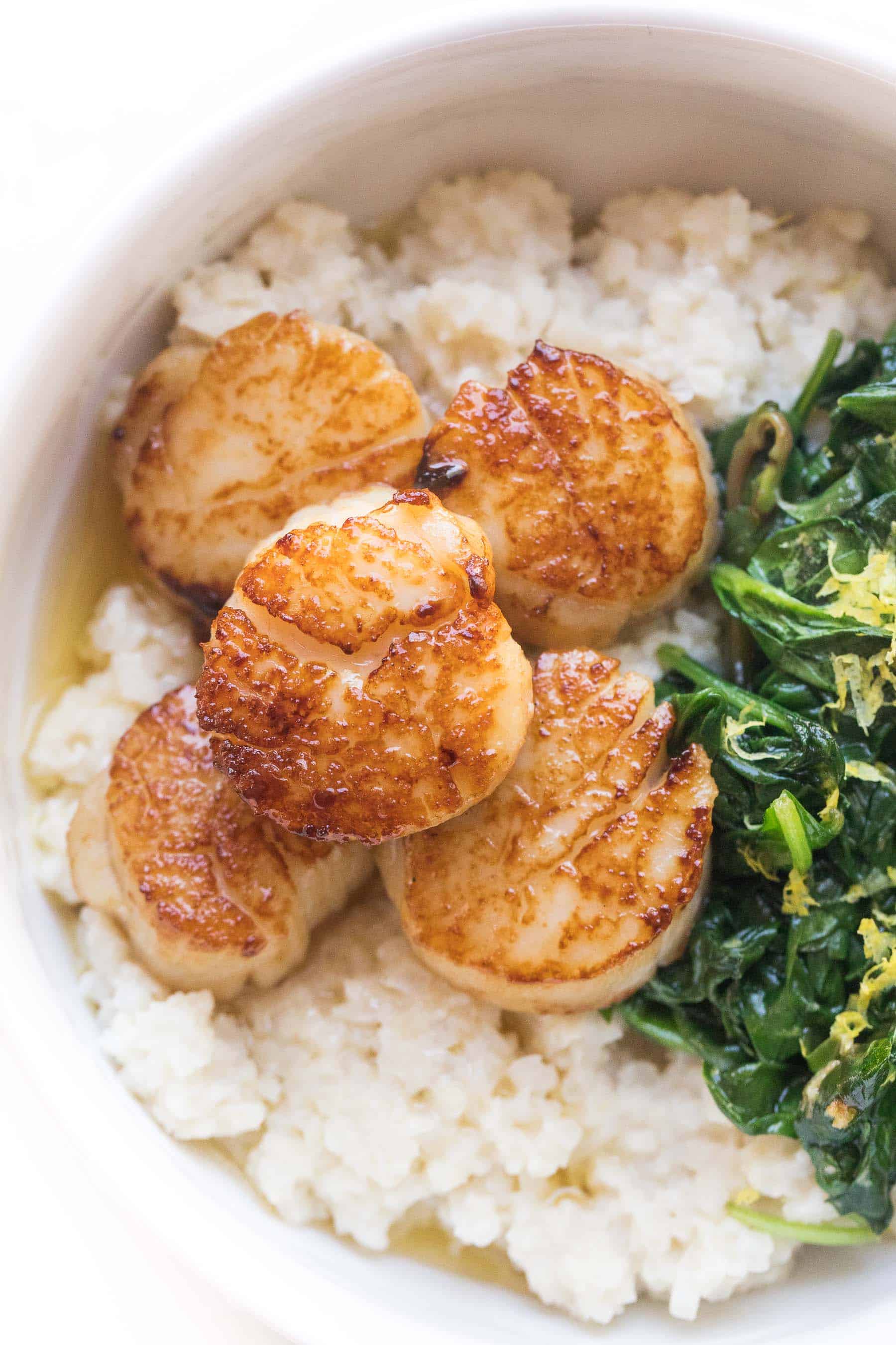 Seared scallops in a white bowl with cauliflower rice risotto + sauteed spinach