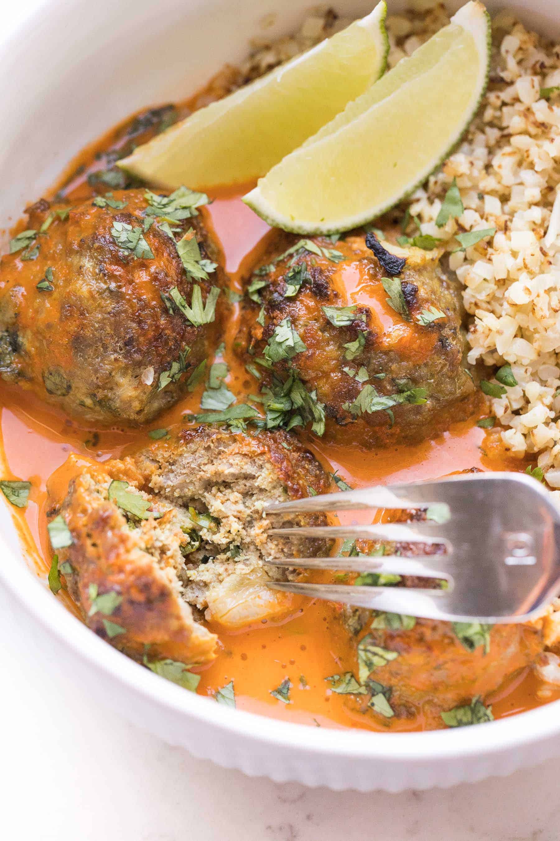 fork cutting thai curry meatballs in a white bowl with thai curry sauce