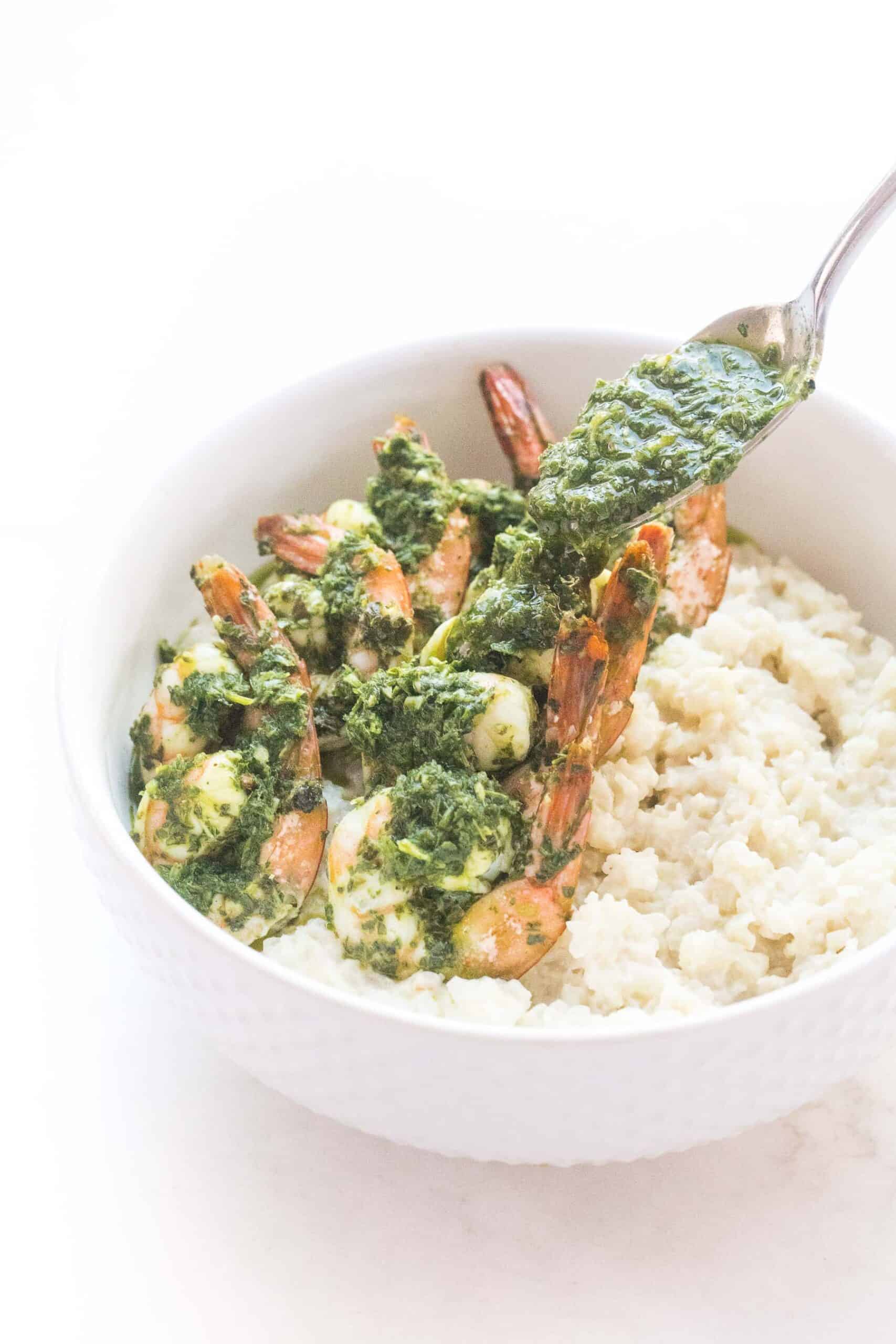 pouring chimichurri on shrimp on cauliflower rice risotto