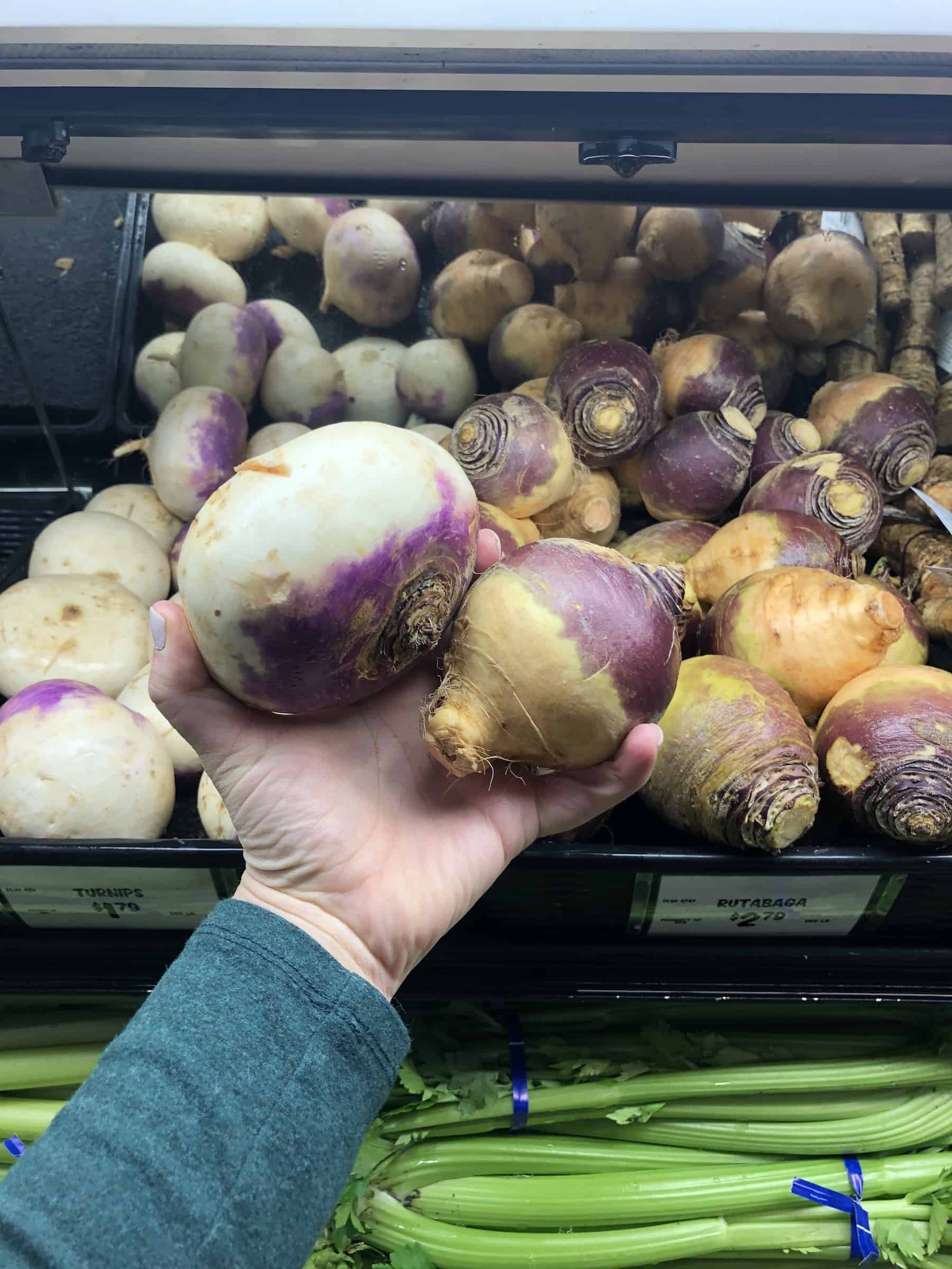 turnips and rutabagas being held in a hand at a grocery store