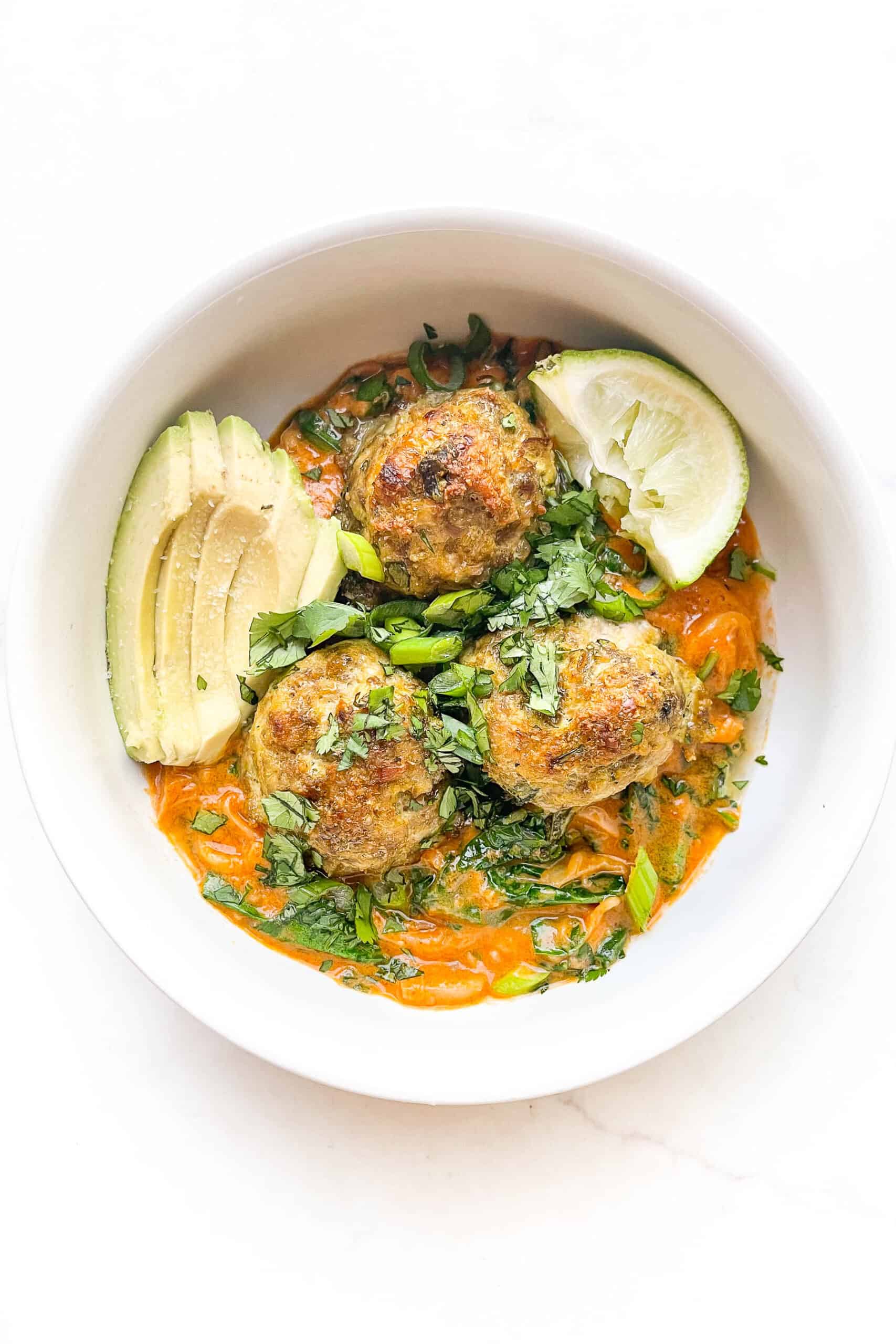 thai curry meatballs over noodles and curry sauce in a white bowl