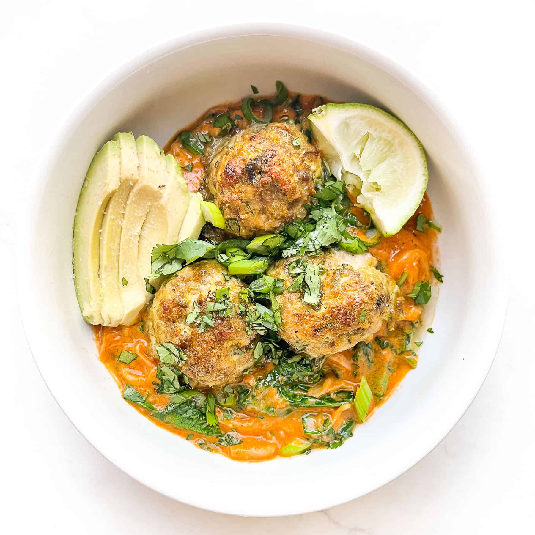 thai curry meatballs over noodles and curry sauce in a white bowl