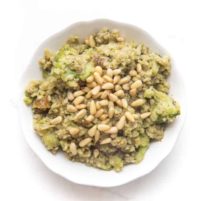 pesto cauliflower rice, broccoli, meatballs and pinenuts in a white bowl
