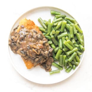 breaded chicken with mushroom gravy on a white plate with green beans