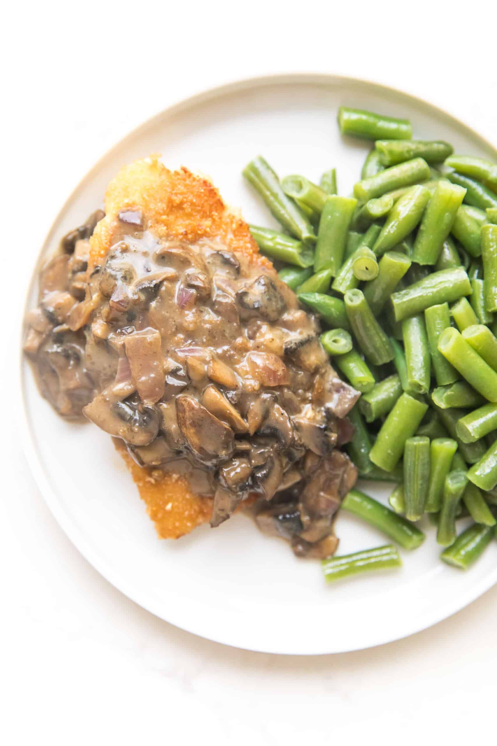 breaded chicken with mushroom gravy on a white plate with green beans