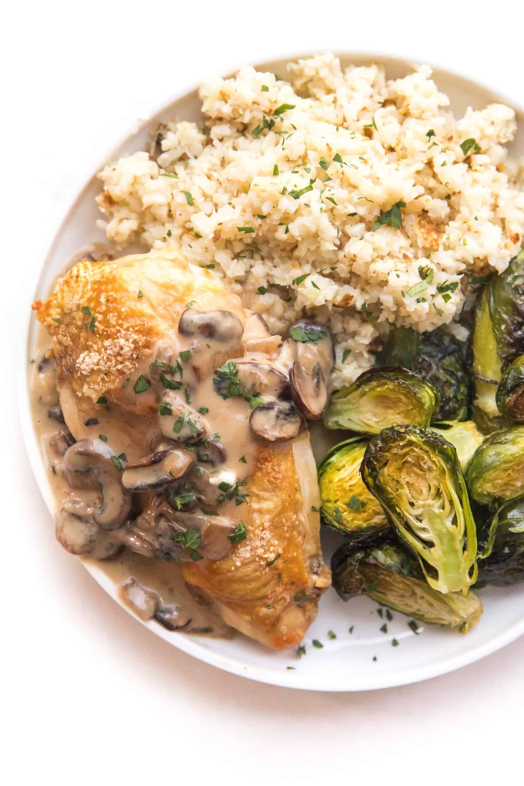 chicken with mushroom gravy on a white plate and background with roasted brussels sprouts and cauliflower rice