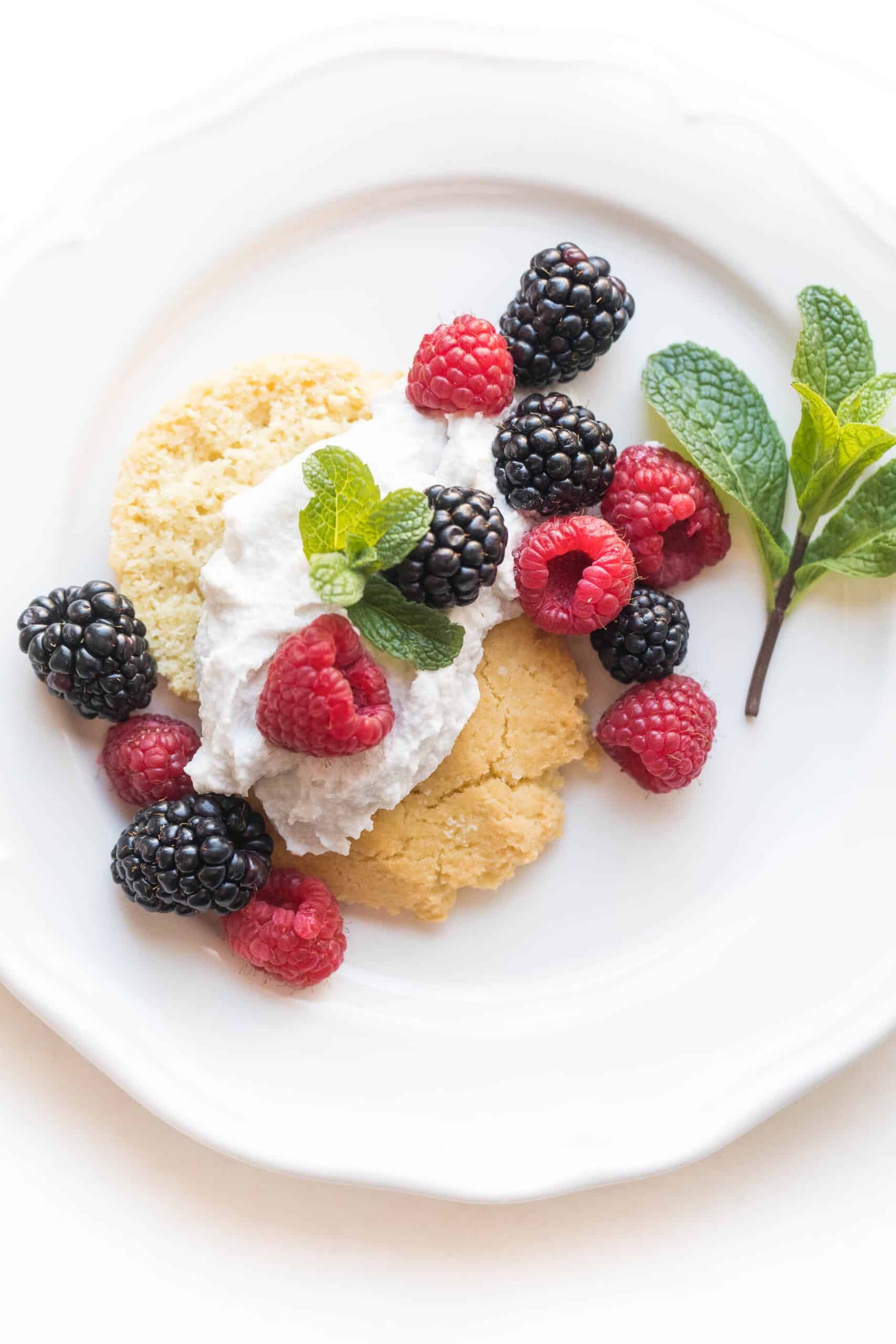 keto berry shortcake biscuit topped with whipped cream and raspberries and blackberries and mint on a white plate