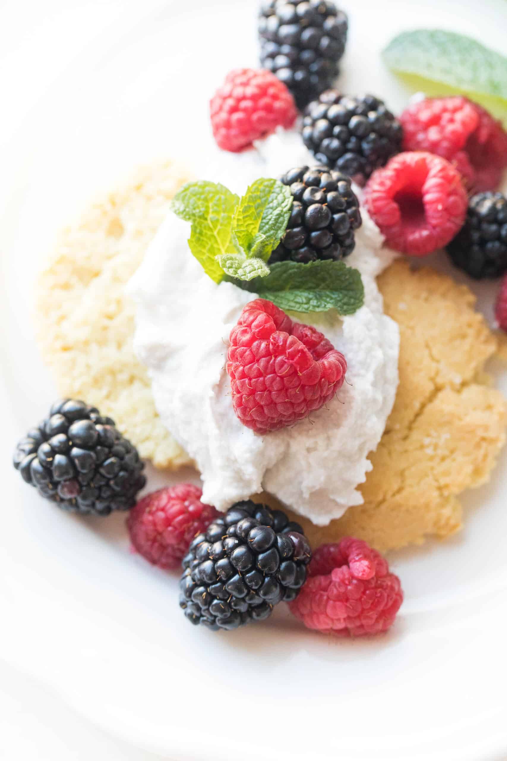 keto berry shortcake biscuit topped with whipped cream and raspberries and blackberries and mint on a white plate