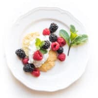 keto berry shortcake biscuit topped with whipped cream and raspberries and blackberries and mint on a white plate