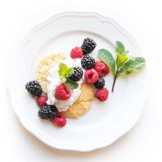 keto berry shortcake biscuit topped with whipped cream and raspberries and blackberries and mint on a white plate