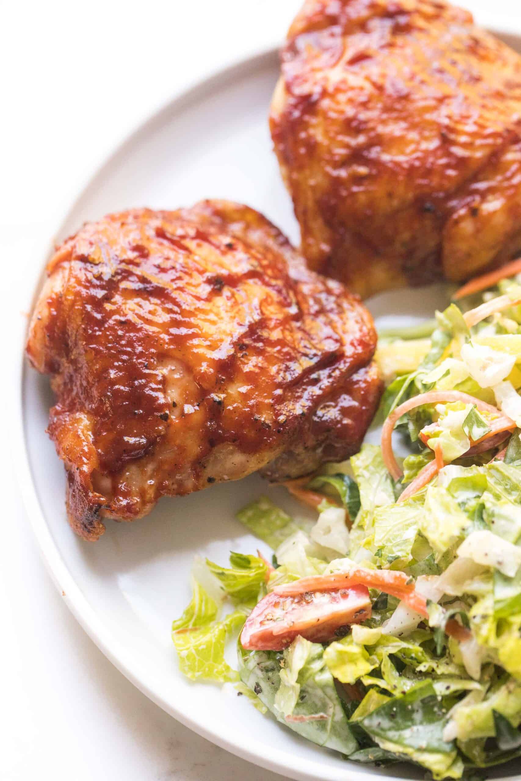 bbq chicken thighs on a white plate with a green salad