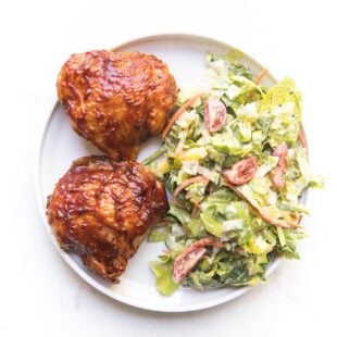 bbq chicken thighs on a white plate with a green salad