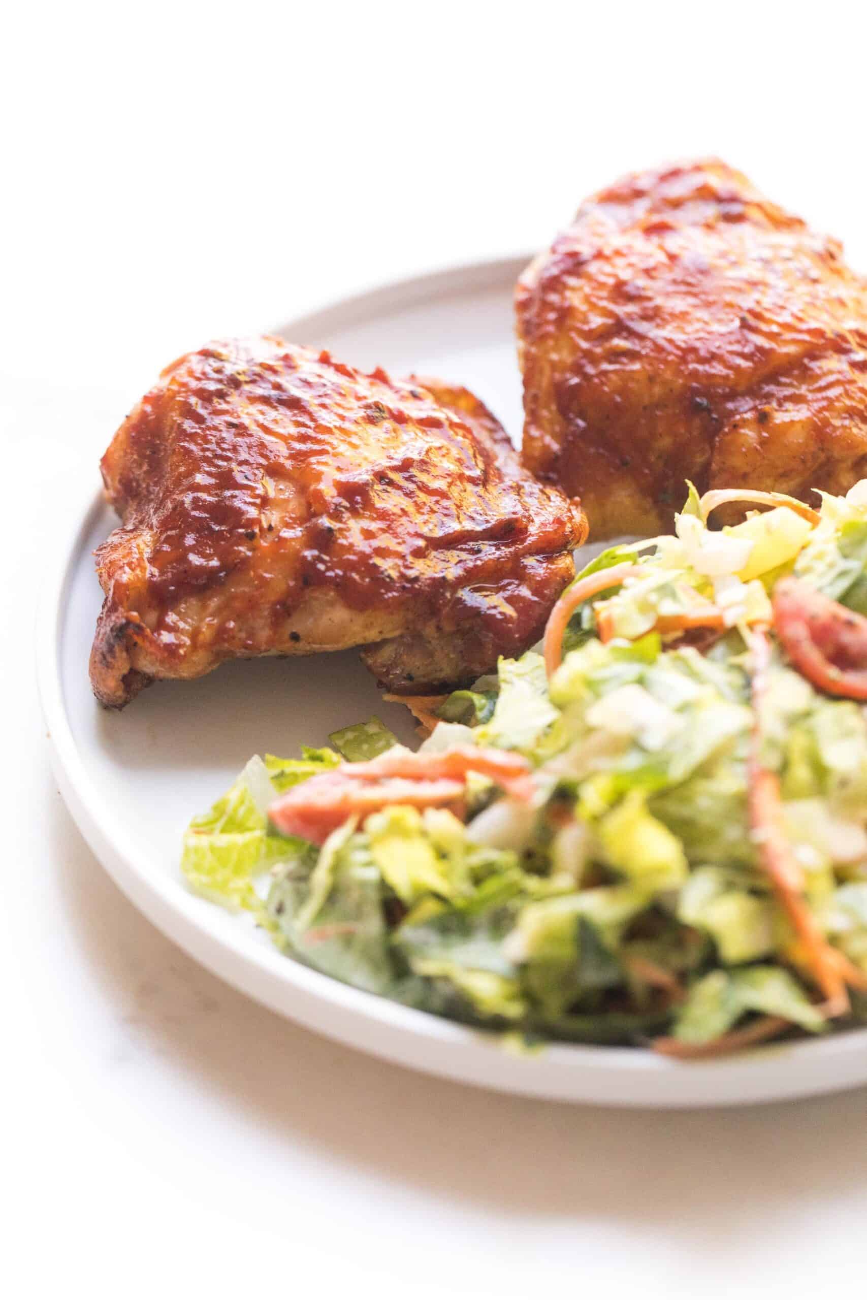 bbq chicken thighs on a white plate with a green salad