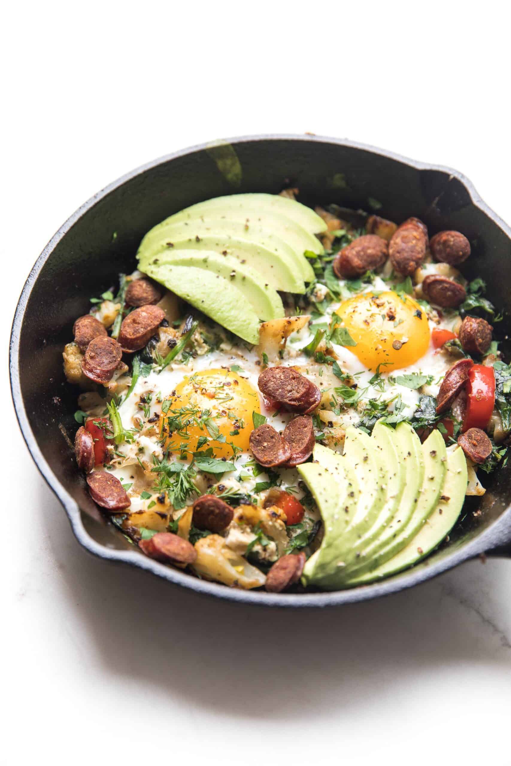 KETO low carb no potato breakfast hash with eggs and avocado in a cast iron skillet on a white background