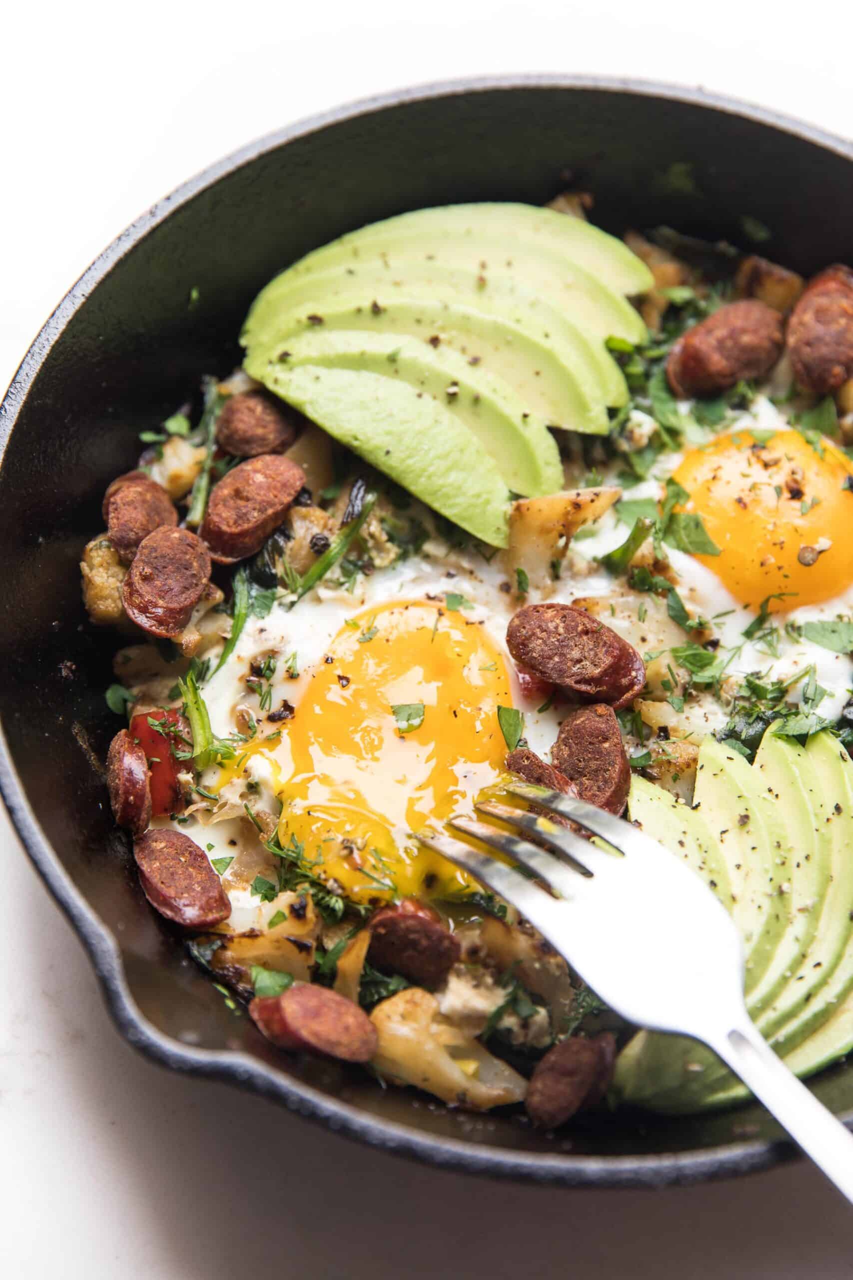 KETO low carb no potato breakfast hash with eggs and avocado in a cast iron skillet on a white background