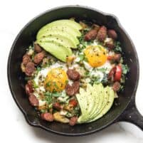 KETO bajo en carbohidratos sin patata hash de desayuno con huevos y aguacate en una sartén de hierro fundido sobre un fondo blanco.