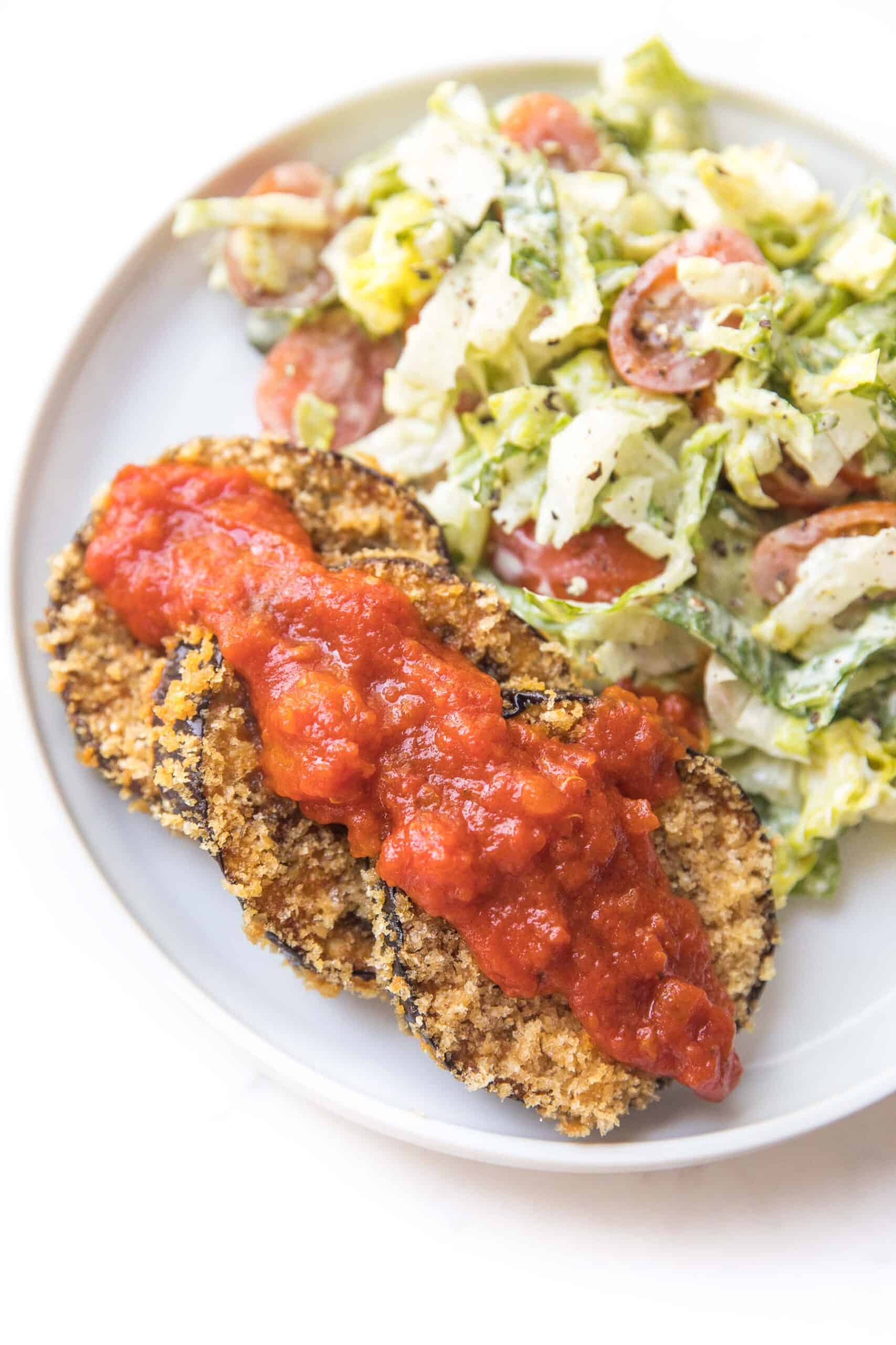 crispy coated eggplant next to caesar salad on a white plate