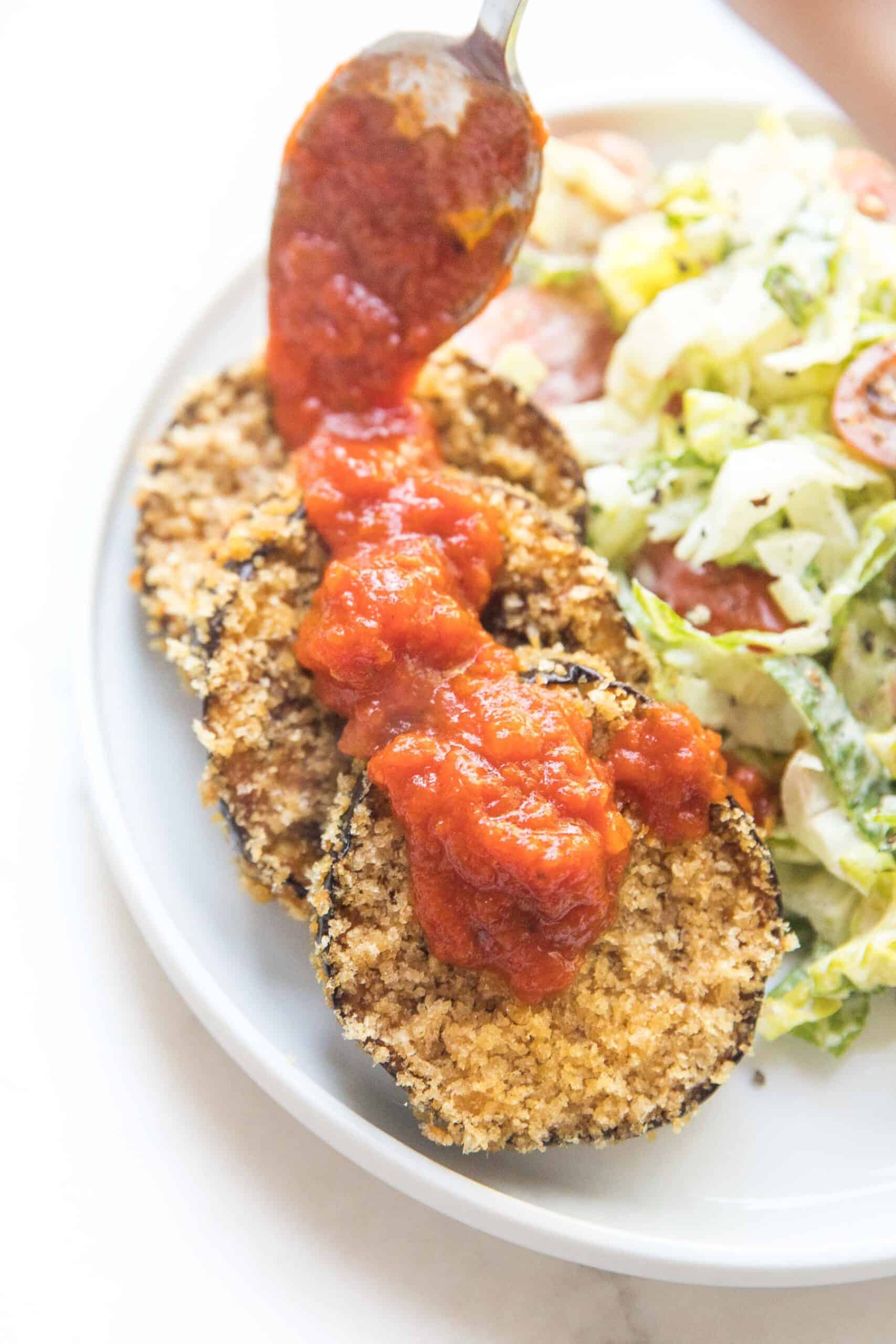 crispy coated eggplant next to caesar salad on a white plate