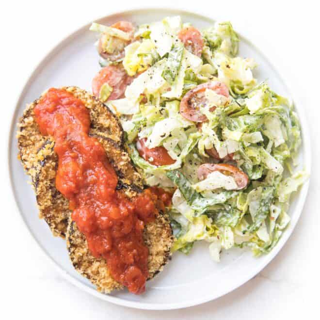 crispy coated eggplant next to caesar salad on a white plate