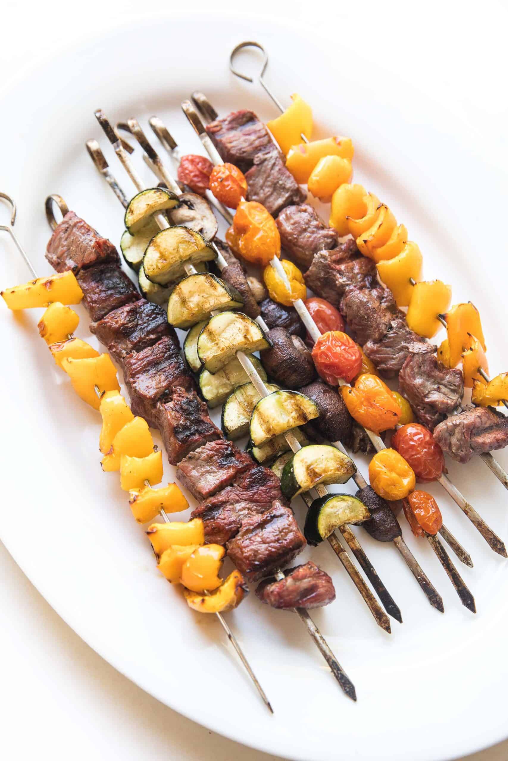 grilled steak and vegetable kabob skewers on a white platter