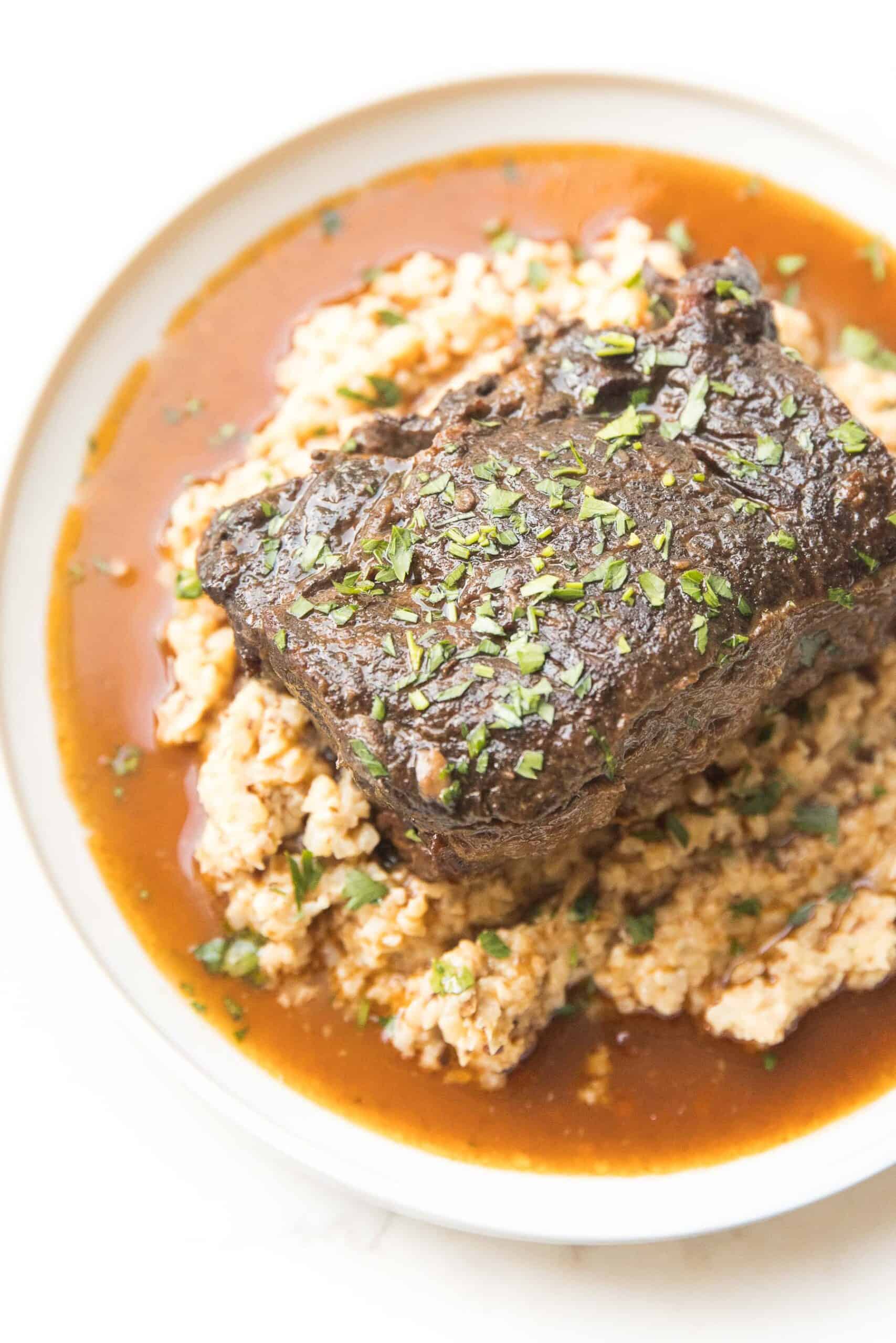 SHORT RIBS AND CAULIFLOWER RICE RISOTTO ON A WHITE PLATE AND BACKGROUND