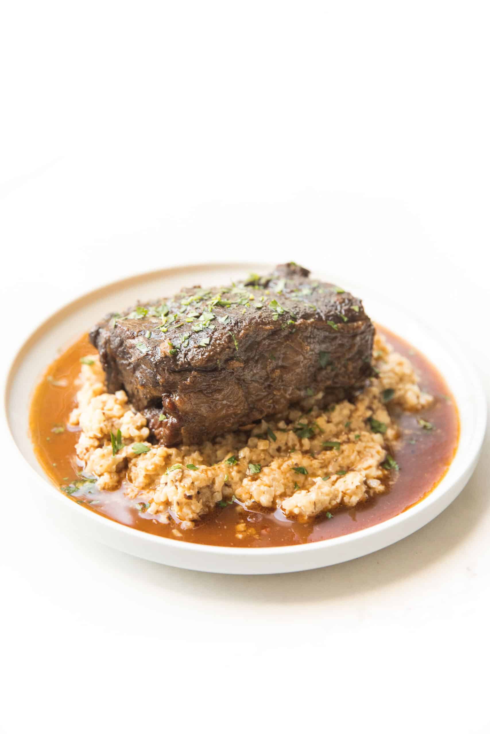 BRAISED SHORT RIBS OVER CAULIFLOWER RICE RISOTTO ON A WHITE PLATE AND BACKGROUND