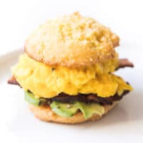 keto biscuit breakfast sandwich with egg, bacon and avocado on a white plate and background