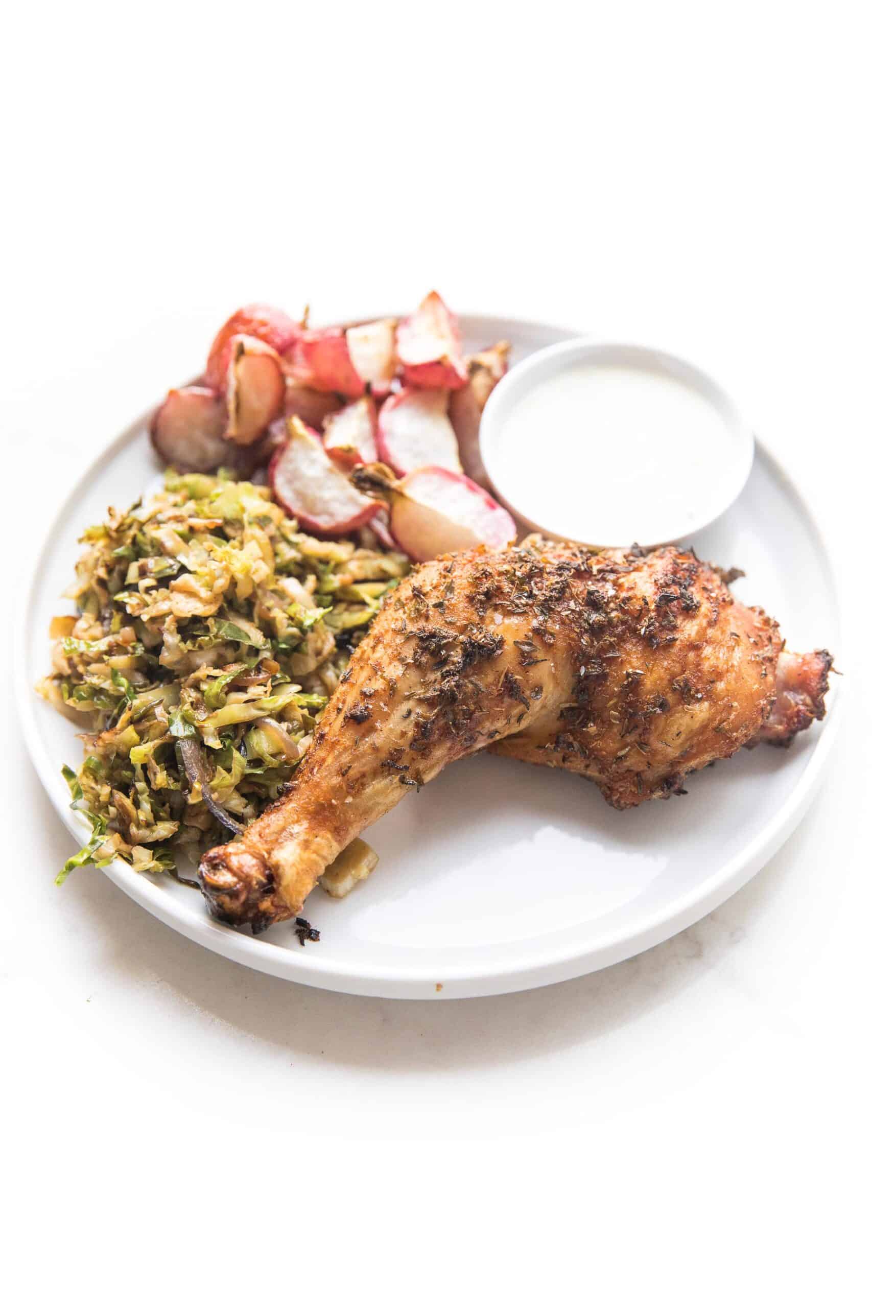 grilled blackened chicken on a white place with roasted radishes and shaved brussels