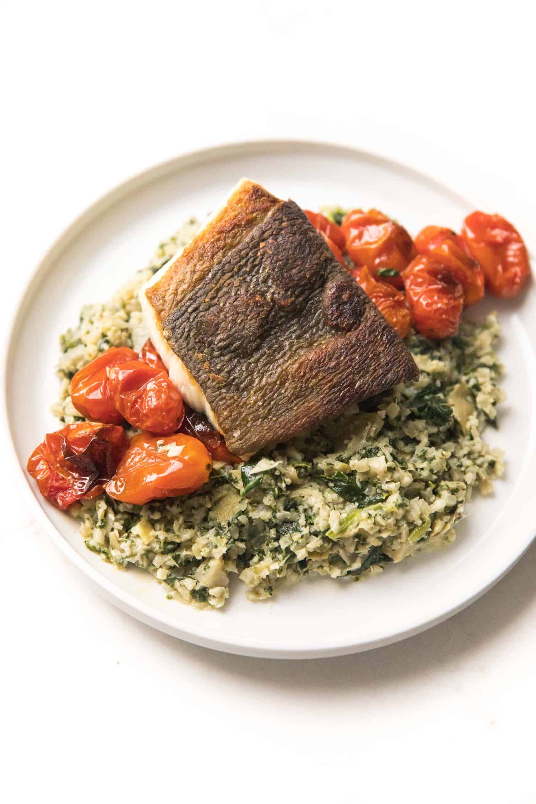 Whole30 + Keto Halibut with Spinach Artichoke Cauliflower Rice Risotto + blistered tomatoes on a white plate