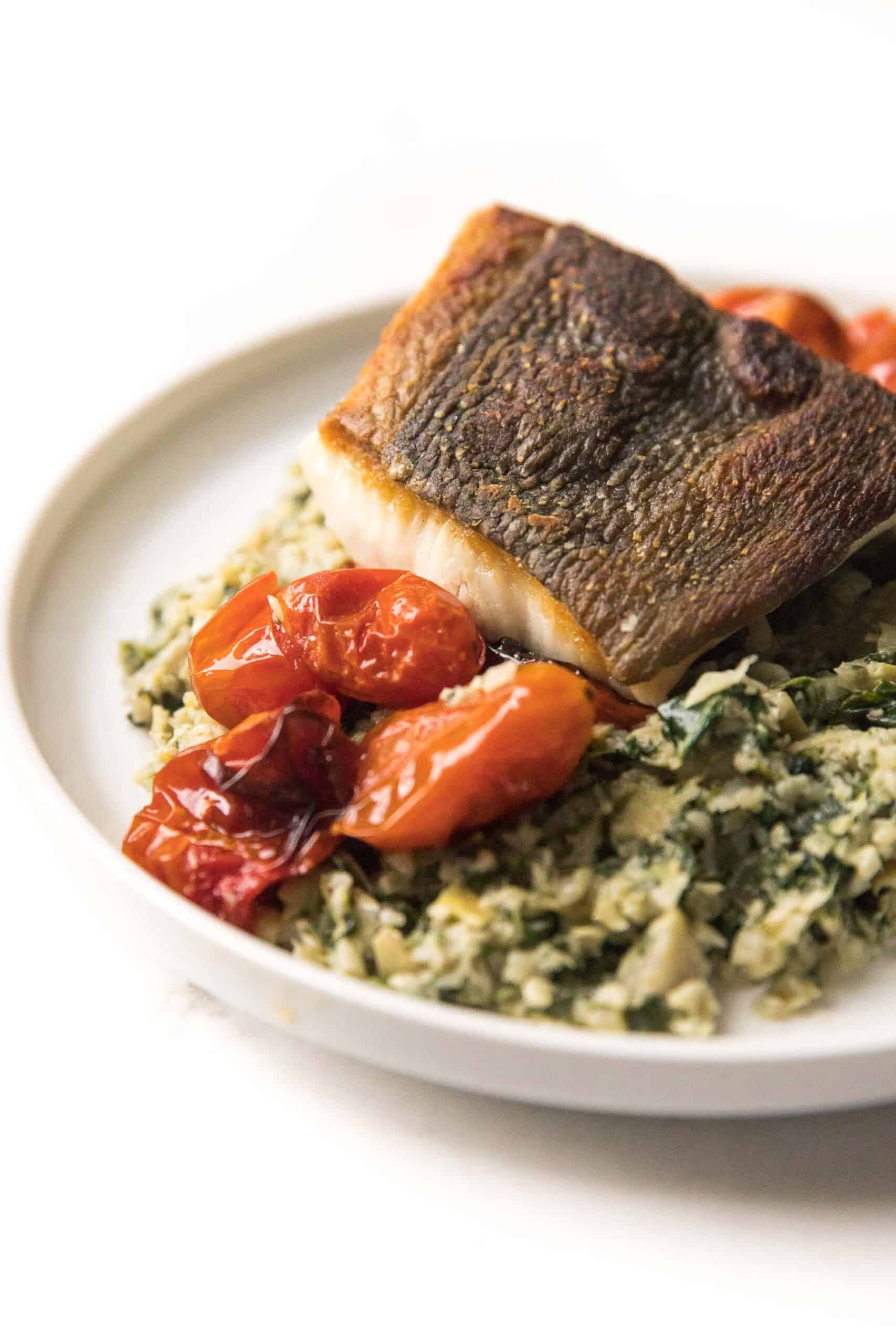 Whole30 + Keto Halibut with Spinach Artichoke Cauliflower Rice Risotto + blistered tomatoes on a white plate