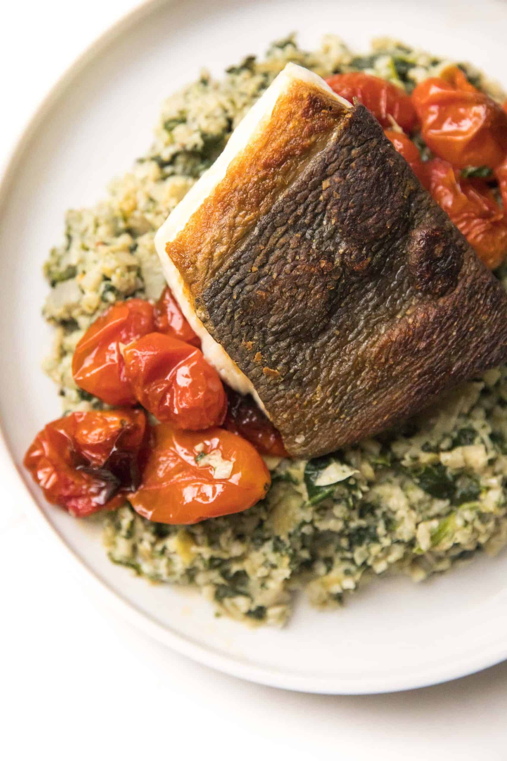 Whole30 + Keto Halibut with Spinach Artichoke Cauliflower Rice Risotto + blistered tomatoes on a white plate