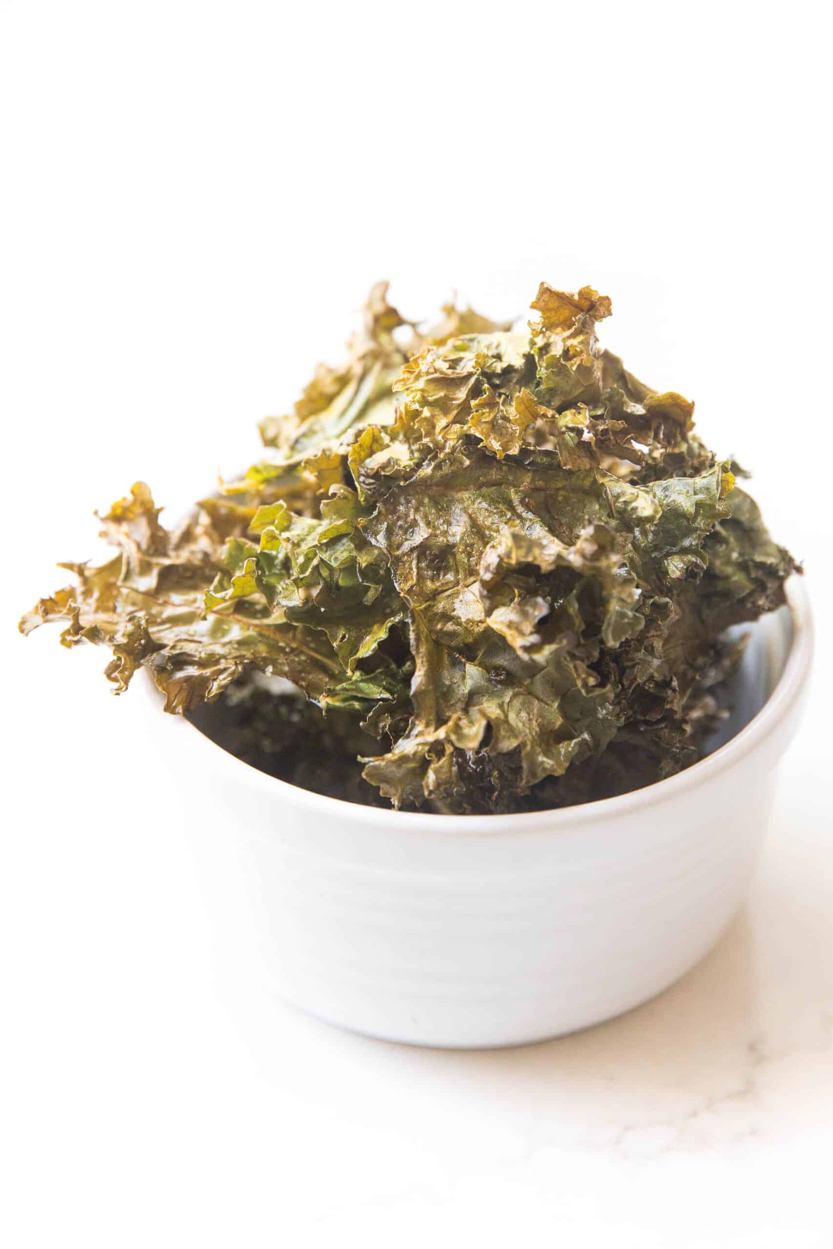 crispy kale chips in a white bowl in a white background