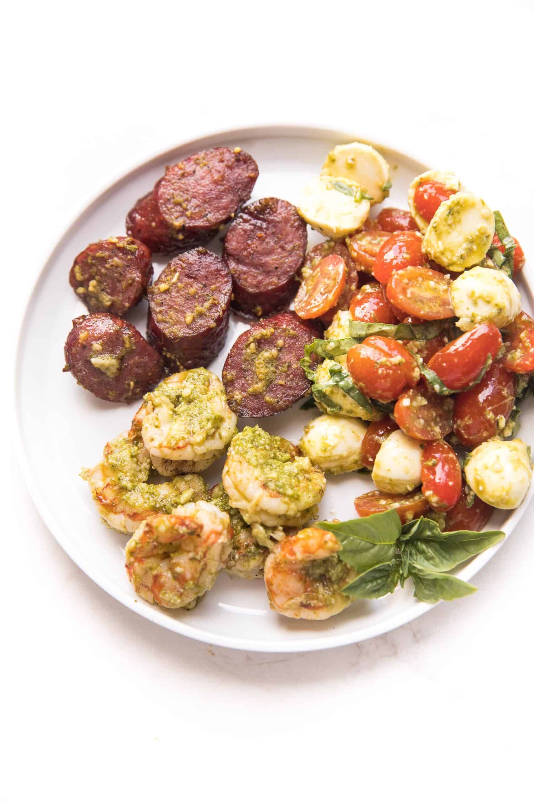 pesto shrimp, sausage and pesto caprese salad on a white plate